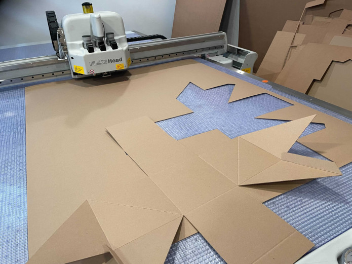 Image contains a photo of a machine cutting a cardboard box.