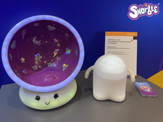 Image contains a photo of Snorble® next to their Lullapod™ with business cards and a sign.